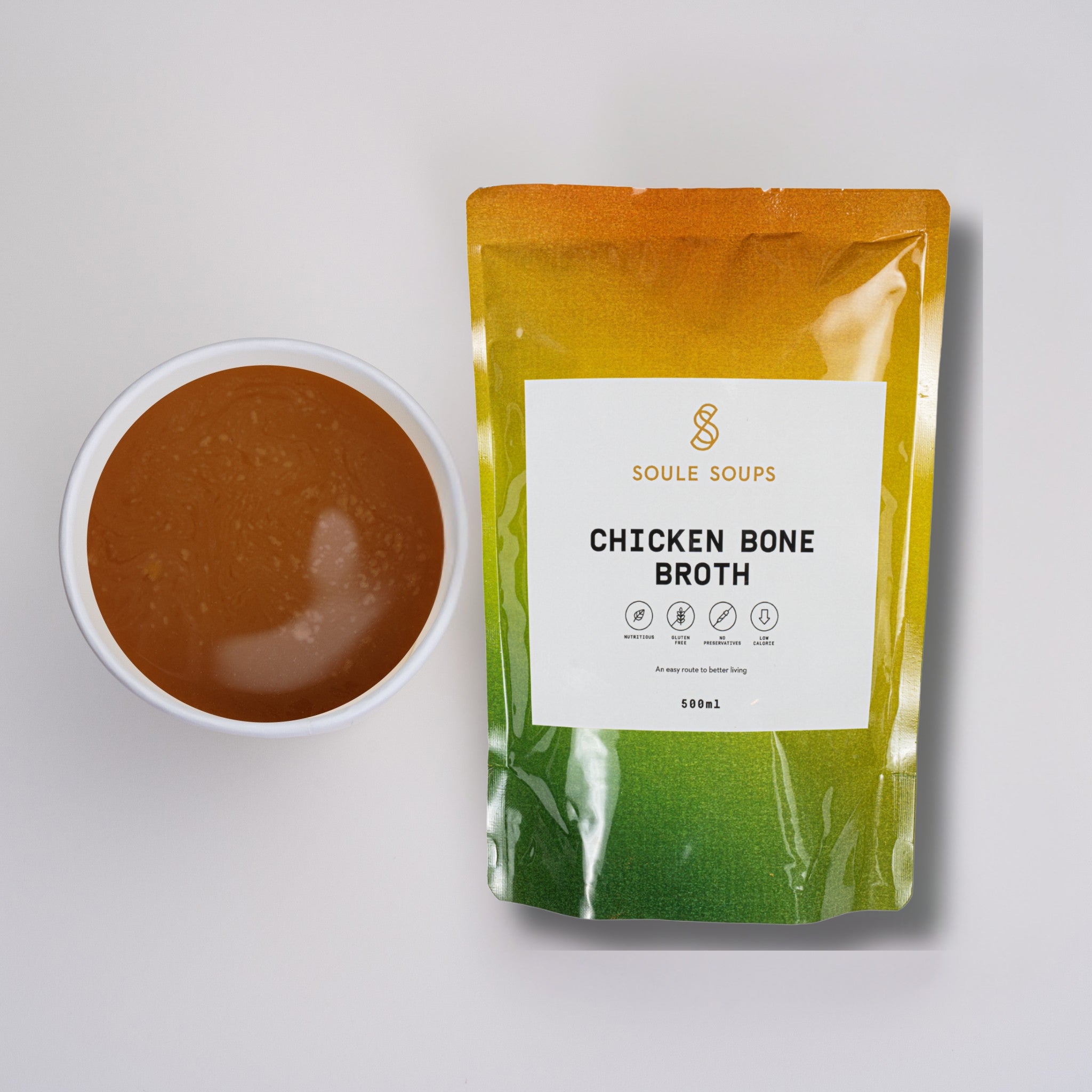 Packaged chicken bone broth with a bowl of broth on a light gray background